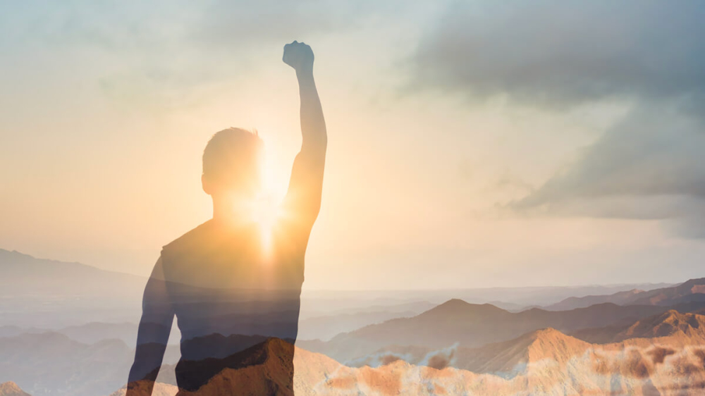 man with his fist in the air, looking over a mountain range