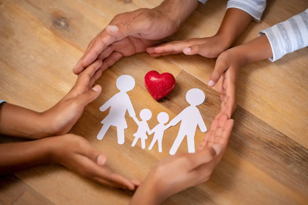 hands surrounding a heart and paper cutout of a family
